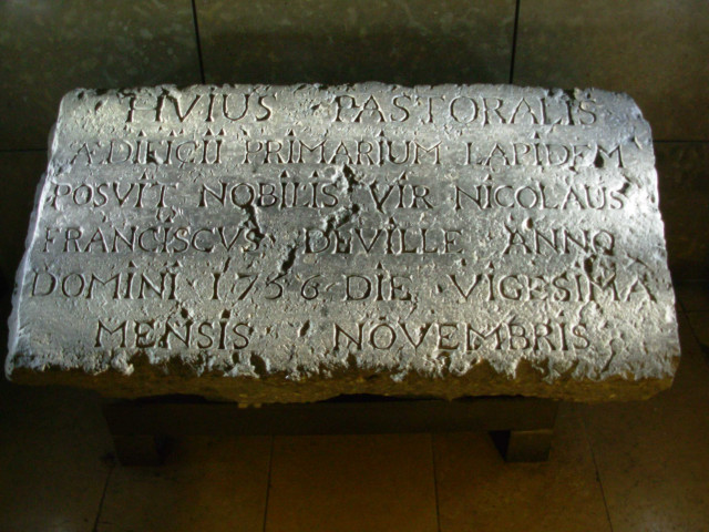 Bloc de pierre noire avec une inscription latine gravée : « le noble seigneur Nicolas François Deville a posé la première pierre de cet édifice pastoral le vingtième jour du mois de novembre de l'an de grâce 1756 ».